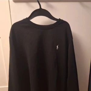Svart tröja från Polo Ralph Lauren - Säljer en stilren svart tröja från Polo Ralph Lauren med en liten broderad logotyp på bröstet. Perfekt för en avslappnad och klassisk look.