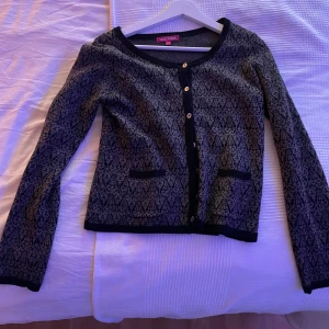 Mönstrad kofta från Indiska - Snygg mönstrad kofta från Bershka i svart och grått. Den har långa ärmar och knappar framtill. Perfekt för att lägga till lite stil i din garderob.