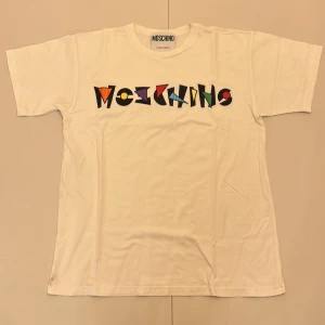 Vit t-shirt från Moschino - Snygg vit t-shirt från Moschino med färgglatt tryck på framsidan. . Klassisk passform och kortärmad design. Skriv om ni har frågor