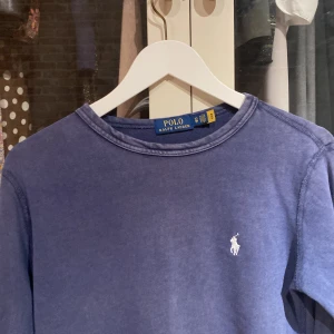 Blå tröja från Polo Ralph Lauren - Säljer en stilren blå tröja från Polo Ralph Lauren med det klassiska logotypbroderiet på bröstet. Tröjan har långa ärmar och en rund halsringning, perfekt för en avslappnad look.
