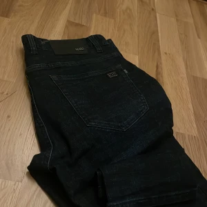 Svarta jeans från Hugo Boss - Snygga svarta jeans från Hugo Boss med klassisk design. Perfekta för en stilren look. De har en bakficka med märkets logga och är tillverkade i ett slitstarkt material.