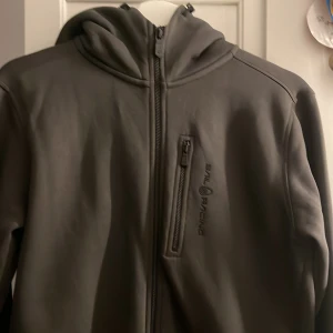 Grå jacka från Sail Racing - Snygg grå jacka från Sail Racing med dragkedja och huva. Perfekt för kyligare dagar med sin stilrena design och praktiska ficka på bröstet.