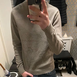 Beige stickad tröja - Säljer en stilren beige stickad tröja med ribbade muddar vid ärmslut och nederkant. Perfekt för kyligare dagar och enkel att matcha med olika outfits. Skick 9/10 väldigt fin använd Max 3 gånger 