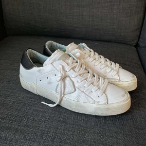 Vita sneakers från Philippe Model - Snygga vita sneakers från Philippe Model med svarta detaljer på hälen. Skorna har klassisk snörning och en stilren design som passar perfekt till vardags. Sulan är i gummi med bra grepp.