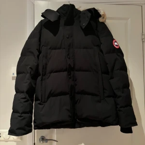 Svart Canada Goose jacka  - Säljer en svart jacka från Canada Goose då den var fel i storleken. Jackan är i modellen Wyndham Parka och har en avtagbar luva med päls som även är avtagbar. Jackan har dragkedja och knappar framtill och fickorna på sidan sängs även med dragkedjor. Den är i nyskick med prislapp fortfarande på. 