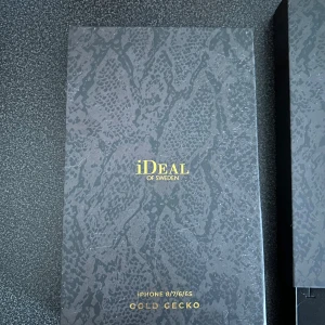 Mobilskal Gold Gecko från iDeal of Sweden - Snyggt oanvänt mobilskal från iDeal of Sweden i modellen Gold Gecko, designat för iPhone 8/7/6/6S. Skalet har ett stilrent mönster som påminner om ormskinn i guld och svart, vilket ger en lyxig känsla. Perfekt för att ge din telefon ett unikt utseende.