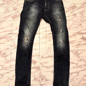 Svarta jeans med slitningar - Snygga svarta jeans med coola slitningar på knäna och låren. Perfekta för en avslappnad stil. De har en klassisk femficksdesign och knappgylf.