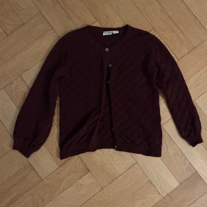 Vinröd kofta från VRS Basic - Säljer en söt vinröd kofta från VRS Basic med ett diskret mönster. Koftan har knappar framtill och långa ärmar. Perfekt för de yngre i familjen! Barn 2 till 4 år!