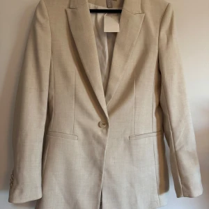 Beige kavaj från H&M - Snygg beige kavaj från H&M med klassisk design och enkel knappstängning. 