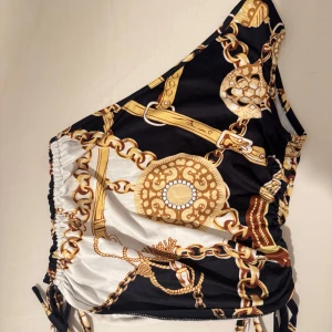 Svart och vit topp med kedjemönster 🖤 - Snygg topp med ett iögonfallande kedjemönster i guld på svart och vit bakgrund. Den har en asymmetrisk design med knytning på sidorna för en justerbar passform. Perfekt för en dejt! 