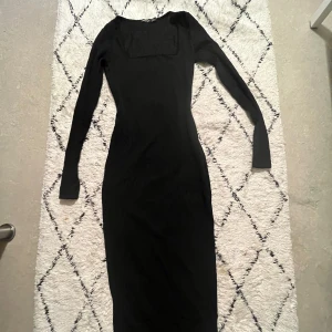Svart långklänning från Boohoo - Elegant svart långklänning från Boohoo med långärmad design. Klänningen har en subtil ribbad textur som ger en extra dimension till det klassiska utseendet. Perfekt för en stilren och sofistikerad look. Den stretchar inte.