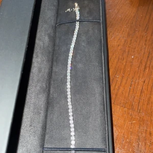 Silverfärgat armband från Kejsar - Elegant silverfärgat armband från Kejsar med gnistrande stenar. Perfekt för att ge en touch av glamour till din outfit. Levereras i en stilren svart förpackning.