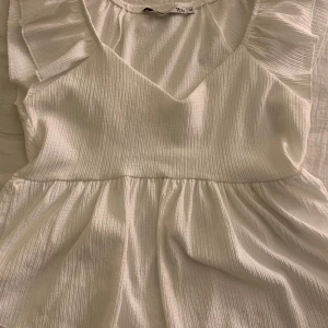 Vit blus från lager 157 - Söt vit blus med volangdetaljer vid axlarna och nere vid magen, perfekt för varma dagar. Använd endast en gång och inte en enda fläck eller beskymmer. Kostar ca 200 kr ny