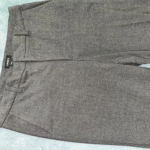 Grå kostymbyxor från Lindex - Snygga grå kostymbyxor från Lindex i en klassisk design. Byxorna har en rak passform med hällor för bälte och diskreta fickor. Perfekta för en stilren look.