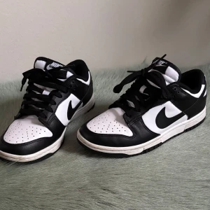Nike Dunk PANDA - Snygga Nike Dunk sneakers i klassisk svart och vit färgkombination. Skorna har en stilren design med snörning och Nike-logga på sidan. Perfekta för en sportig look. Panda 🐼 