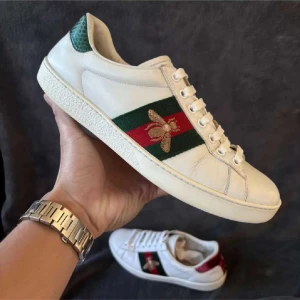 Vita Gucci ace sneakers storlek 41 - Snygga vita sneakers från Gucci med gröna och röda detaljer samt en broderad guldfärgad bi på sidan. Skorna har snörning och en unik design med olika färger på hälen, grön och röd. Priset går att diskutera. Vid frågor och funderingar så hör av dig till mig! Mvh Axel