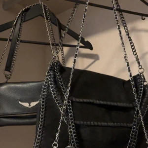 Svart axelväska med kedjedetaljer❤️‍🔥 - Snygg svart axelväska i mocka med kedjedetaljer. Väskan har en stilren design med en kedja som axelrem och en dekorativ kedja längs kanterna. Perfekt för att ge en edgy touch till din outfit. Den är prefekt till skolan och gymmet💕och den är knappt använd. Köpt för 600kr🌺❤️‍🔥Jag köpte här på plick.