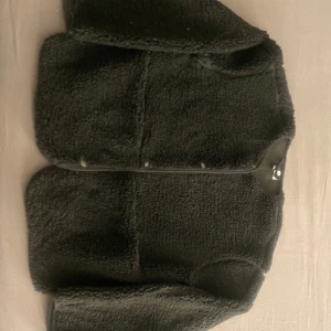 Svart teddyjacka från h&m - Mysig svart teddyjacka från h&m i storlek XXS. Perfekt för att hålla värmen under kyliga dagar. jackan har en enkel design med knappar framtill.