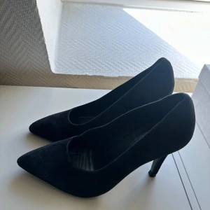 Svarta pumps från Filippa K - Eleganta svarta pumps från Filippa K i storlek 37. Skorna har en spetsig tå och är tillverkade i mocka, vilket ger en lyxig känsla. Perfekta för en stilren look.