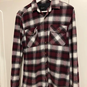 Rutig flanellskjorta från Vailent - Snygg rutig flanellskjorta i vinrött, svart och vitt från Vailent. Skjortan har långa ärmar och två bröstfickor med knappar. Perfekt för en avslappnad stil.