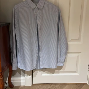 Randig skjorta från Mango - Snygg och klassisk blå- och vitrandig skjorta från Mango, aldrig använd. Skjortan har långa ärmar och knappar framtill. Perfekt för en stilren look.