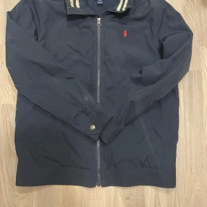 Polo Ralph Lauren jacka - Snygg svart jacka från Polo Ralph Lauren med dragkedja och klassisk krage. Den är i storleken  extra Large men passar runt 165-175cm. Stilren och perfekt innan vintern och mot våren