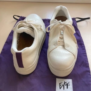 Vita sneakers från Eytys - Snygga vita sneakers från Eytys med lila detalj på hälen. Skorna har en klassisk snörning och en robust sula. Perfekta för en stilren look.
