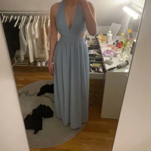 Ljusblå balklänning med öppen rygg - Elegant ljusblå långklänning med djup v-ringning och öppen rygg. Klänningen har ett korsat band i ryggen och är ärmlös, vilket ger en stilren och luftig känsla. Jag är 173cm lång