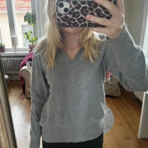 Grå stickad tröja - Säljer en mysig grå stickad tröja med v-ringning. Tröjan har långa ärmar och ribbstickade muddar vid ärmslut och nederkant. Perfekt för kyliga dagar!