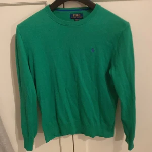 Grön tröja från Polo Ralph Lauren - Snygg grön tröja från Polo Ralph Lauren med broderad logga på bröstet. Tröjan har en klassisk rund hals och långa ärmar, perfekt för en stilren look. Passar Xs men är 14-16 år