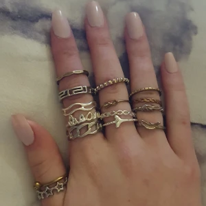 Set med olika ringar i silver och guld - Ett set med flera stilrena ringar i både silver och guld. Designen varierar med detaljer som kedjor, blad och geometriska former. Perfekt för att mixa och matcha för en personlig stil. Köpta från olika märken och priser men säljer alla tillsammans för billigt.
