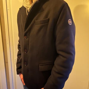 Colmar jacka/kavaj/overshirt - Snygg svart fodrad overshirt från Colmar med knappar och dragkedja. Den är otroligt varm och håller kylan bra i vinter. Den har en klassisk design med tre fickor framtill och en diskret logga på ärmen. Perfekt för en stilren look. Jackan är varm och perfekt nu till vintern när man vill klä upp sig. Hör av dig vid frågor, pris kan såklart diskuteras vid snabb affär!