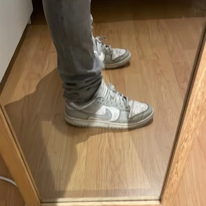 Nike skor  - Säljer ett par klassiska Nike Dunk sneakers i vitt och grått. Storlek 42,5, skorna är använda och är inte i ett super bra skick men jag skulle säga att dom funkar och jag säljer dom för ett lågt pris eftersom dom inte är i topp skick! Skriv för frågor eller funderingar.