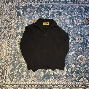 Svart jacka från Corteiz - Snygg svart jacka från Corteiz med broderad logga på bröstet. Jackan har dragkedja och långa ärmar, perfekt för en stilren look. Passar bra till både vardag och mer avslappnade tillfällen.   Den är inte använd endast testad skriv till mig privat ifall du skulle vilja ha mer bilder det finns mer detaljer på jackan som inte ficks med på bilderna 