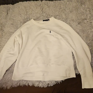 Vit tröja från Polo Ralph Lauren - Säljer en stilren vit tröja från Polo Ralph Lauren med det klassiska broderade logotypen på bröstet. Tröjan har en normal passform och långa ärmar, perfekt för en avslappnad look.