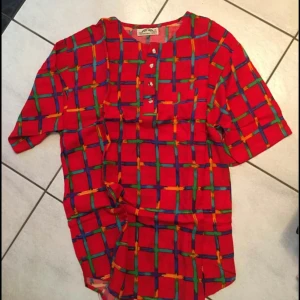 Färgglad henley-skjorta - Säljer en färgglad henley-skjorta med ett rutigt mönster i rött, blått, grönt och gult. Skjortan har korta ärmar och knappar framtill. Perfekt för en unik och livfull stil.