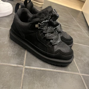 Svarta sneakers från UGG - Snygga svarta sneakers med robust sula och tjocka snören. Skorna har en kombination av textil och syntetmaterial, vilket ger en modern look. Perfekta för en stilren vardagsstil.