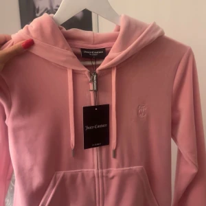 Rosa hoodie från Juicy Couture - Säljer en snygg rosa hoodie från Juicy Couture med dragkedja och huva. Den har en broderad logga på bröstet och praktiska fickor framtill.