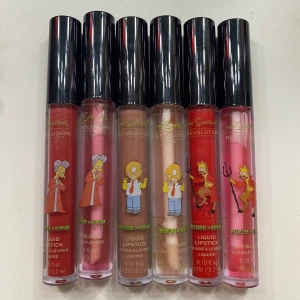 Revolution x The Simpsons Liquid Lipstick Set - Set med sex flytande läppstift från Revolution med The Simpsons-tema. Färgerna varierar från djup röd till ljusrosa, med karaktärer från serien på förpackningen. Varje tub innehåller 3,2 ml.