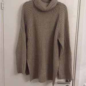 Beige/brun ribbad polotröja - Säljer en mysig beige polotröja med ribbad struktur. Perfekt för kyliga dagar med sin långa ärmar och höga krage. Tröjan är både stilren och bekväm.