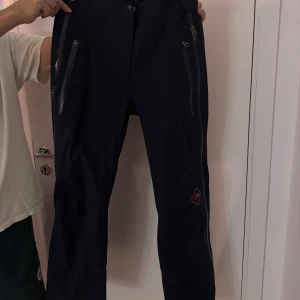 Svarta skidbyxor med dragkedjor från j Lindberg  - Snygga svarta byxor med flera dragkedjor framtill. Perfekta för en modern och stilren look. Byxorna har en normal passform och är tillverkade i ett slitstarkt material. Oanvänd med prislapp kvar, säljer matchande skidjacka 