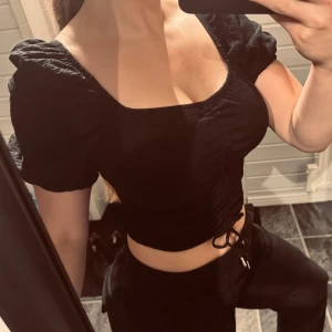 Svart croppad topp med puffärmar - Snygg svart croppad topp med puffiga kortärmar och rynkdetalj framtill. Scrunchen är även justerbar (bild 1&2 så lång den kan bli och bild 3&4 så ihop scrunchad som möjligt)