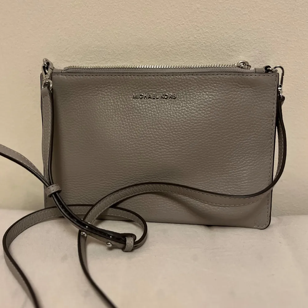Snygg grå axelväska från Michael Kors med justerbar axelrem. Väskan har flera fack och stängs med dragkedja. Perfekt för att hålla ordning på dina saker med stil.. Laukut & Käsilaukut.