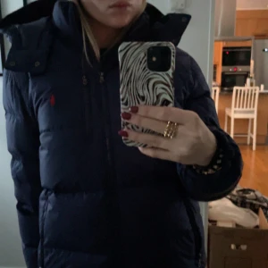Mörkblå dunjacka från Ralph Lauren - INTRESSEKOLL!! En snygg mörkblå dunjacka från Ralph Lauren med dragkedja och huva. Jackan har en broderad logotyp på bröstet och långa ärmar. Perfekt för kyliga dagar!