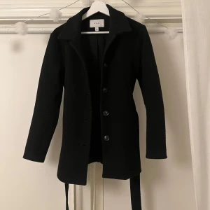 Svart kappa från VILA - Elegant svart kappa från VILA med knappar med ett band runt midjan som man kan knyta eller låta hänga. Perfekt för kyligare dagar med sin stilrena design och långa ärmar. Pris går att diskuteras, normal i storleken💕