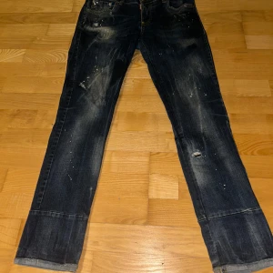 Mörkblå jeans från Dsquared2 - Säljer ett par mörkblå jeans från Dsquared2 med slitna detaljer och en klassisk femficksdesign. Jeansen har en knappgylf och en läderpatch med logotyp på baksidan. Knappt använda.