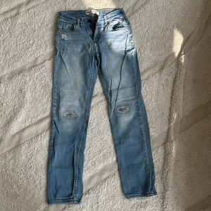 Levi's 512 Slim Taper Jeans - Säljer ett par snygga Levi's 512 Slim Taper jeans i Storlek 12A. De har en cool, sliten look med slitningar vid knäna och en bekväm passform. Perfekta för en avslappnad stil!