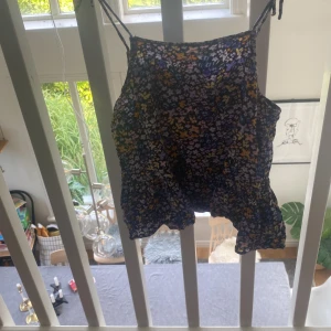 Blommig linne från H&M - Säljer ett superfint blommigt linne från H&M. Det har tunna axelband och ett härligt blommönster i lila, blått och gult. Linnet är i bra skick!🤗