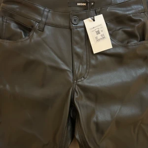 Svarta skinnbyxor från BikBok - Säljer ett par snygga svarta skinnbyxor från BikBok i storlek 38. Byxorna har en tight passform och är gjorda i ett glansigt skinnmaterial. De har fickor både fram och bak samt en knapp och dragkedja i midjan. Varmare material inne i byxan bra till vintern. Aldrig använda 