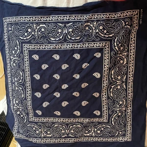 Mörkblå paisleymönstrad halsduk - Säljer en snygg mörkblå bandana med klassiskt paisleymönster i vitt. Perfekt accessoar för att ge din outfit en cool touch. Materialet känns mjukt och skönt mot huden. Passar både till vardags och speciella tillfällen!